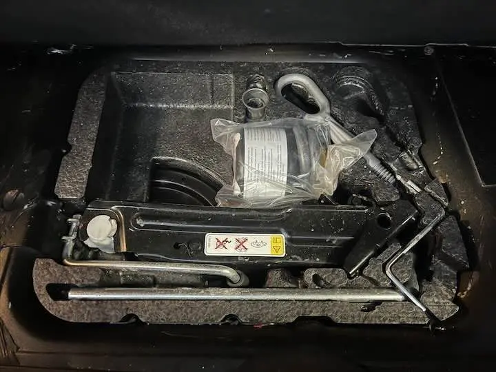 Vue en plongée sur le cric et les outils de bord noirs du coffre d'une MINI Cooper Cabriolet noire de 2012.