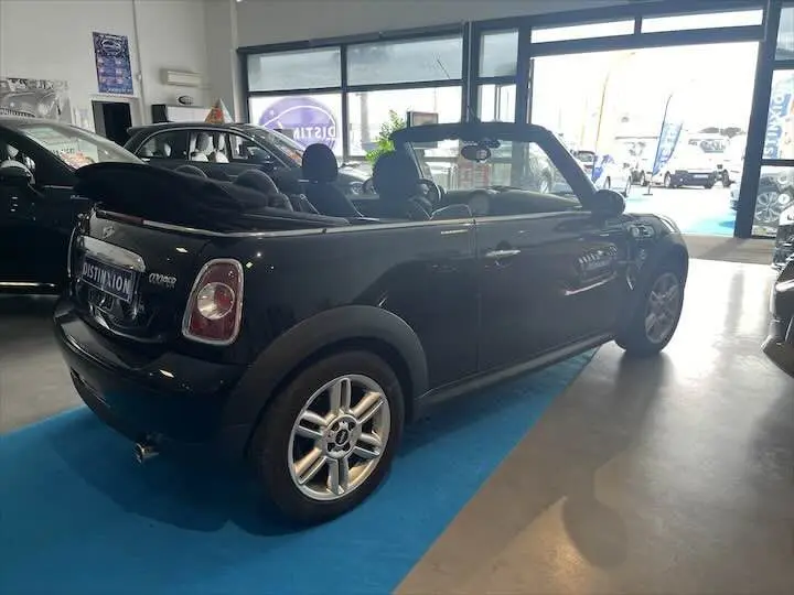 Vue 3/4 arrière droite d'une MINI Cooper Cabriolet noire avec capote ouverte, stationnée en intérieur showroom.