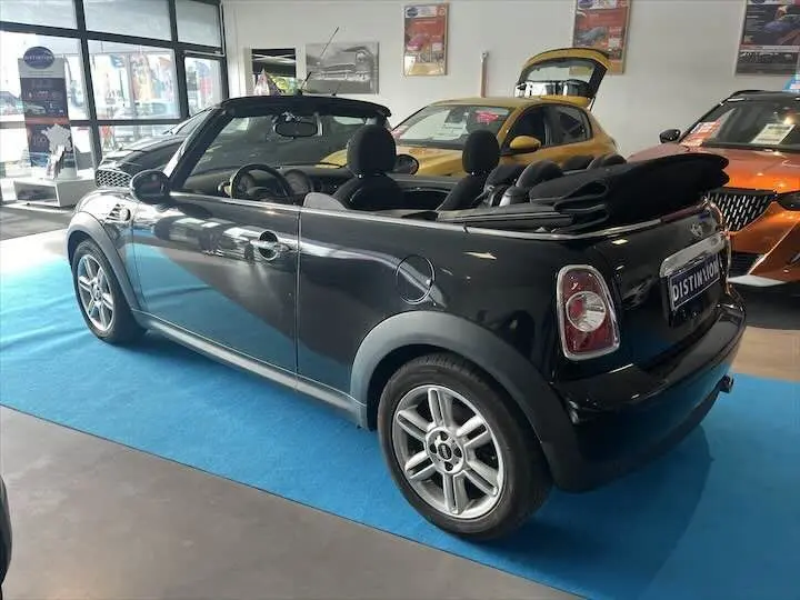 MINI Cooper Cabriolet noire vue de trois quarts arrière droit, capote ouverte, intérieur noir visible en concession.