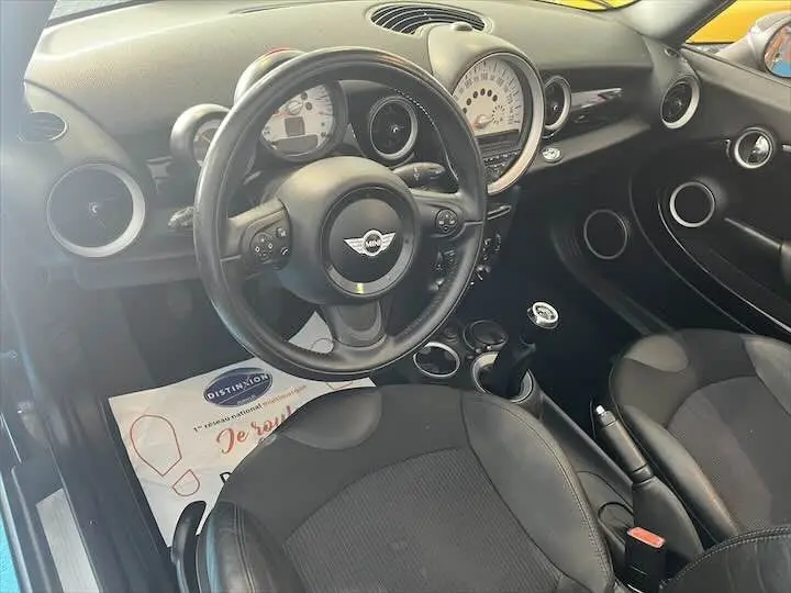 Vue intérieure de la MINI Cooper Cabriolet 2012 noire, montrant le volant, tableau de bord et sièges en tissu et cuir noir.