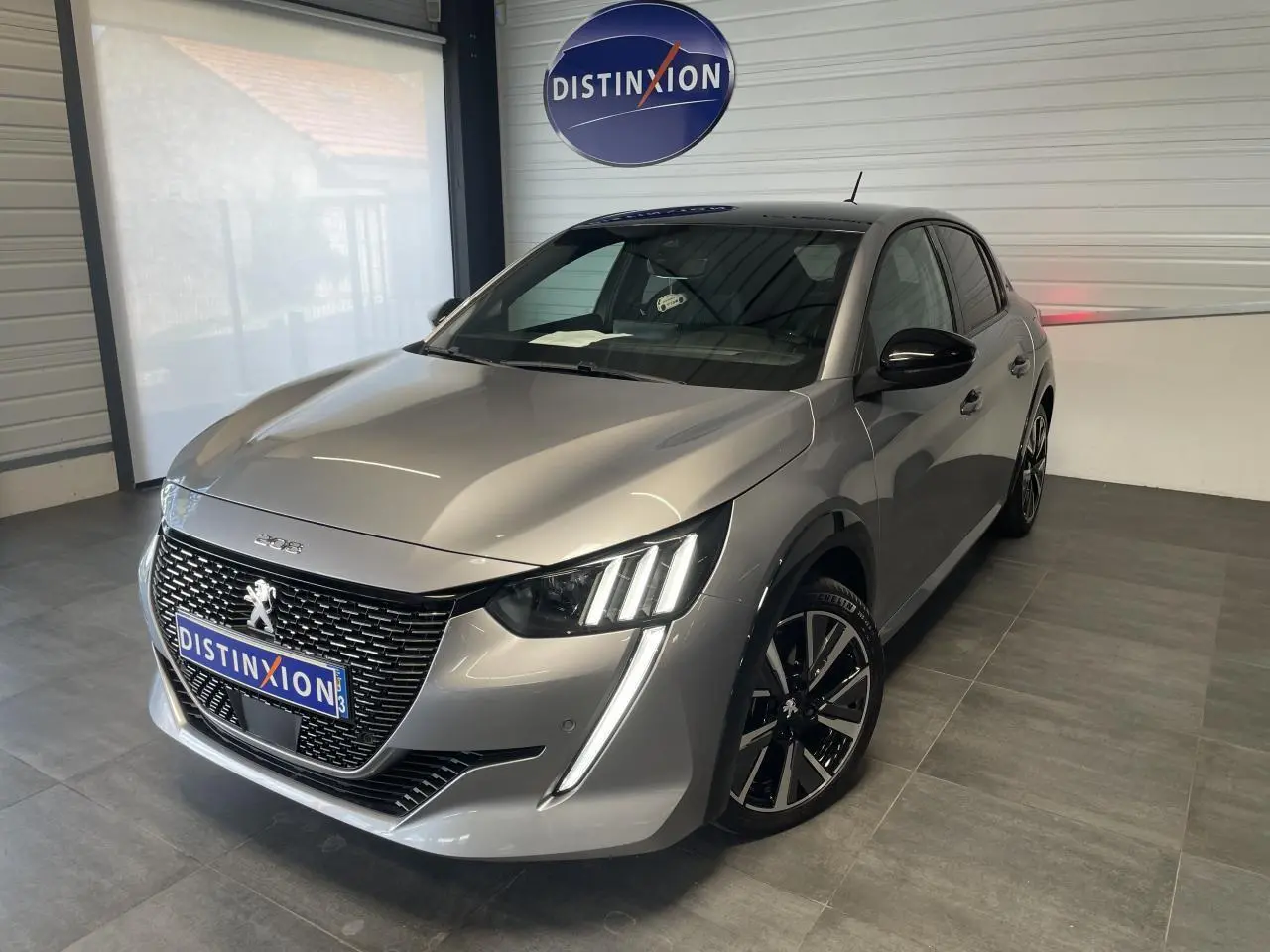 Peugeot 208 gris clair métallisé vue 3/4 avant droit avec toit noir et jantes alliage 17 pouces en intérieur showroom.