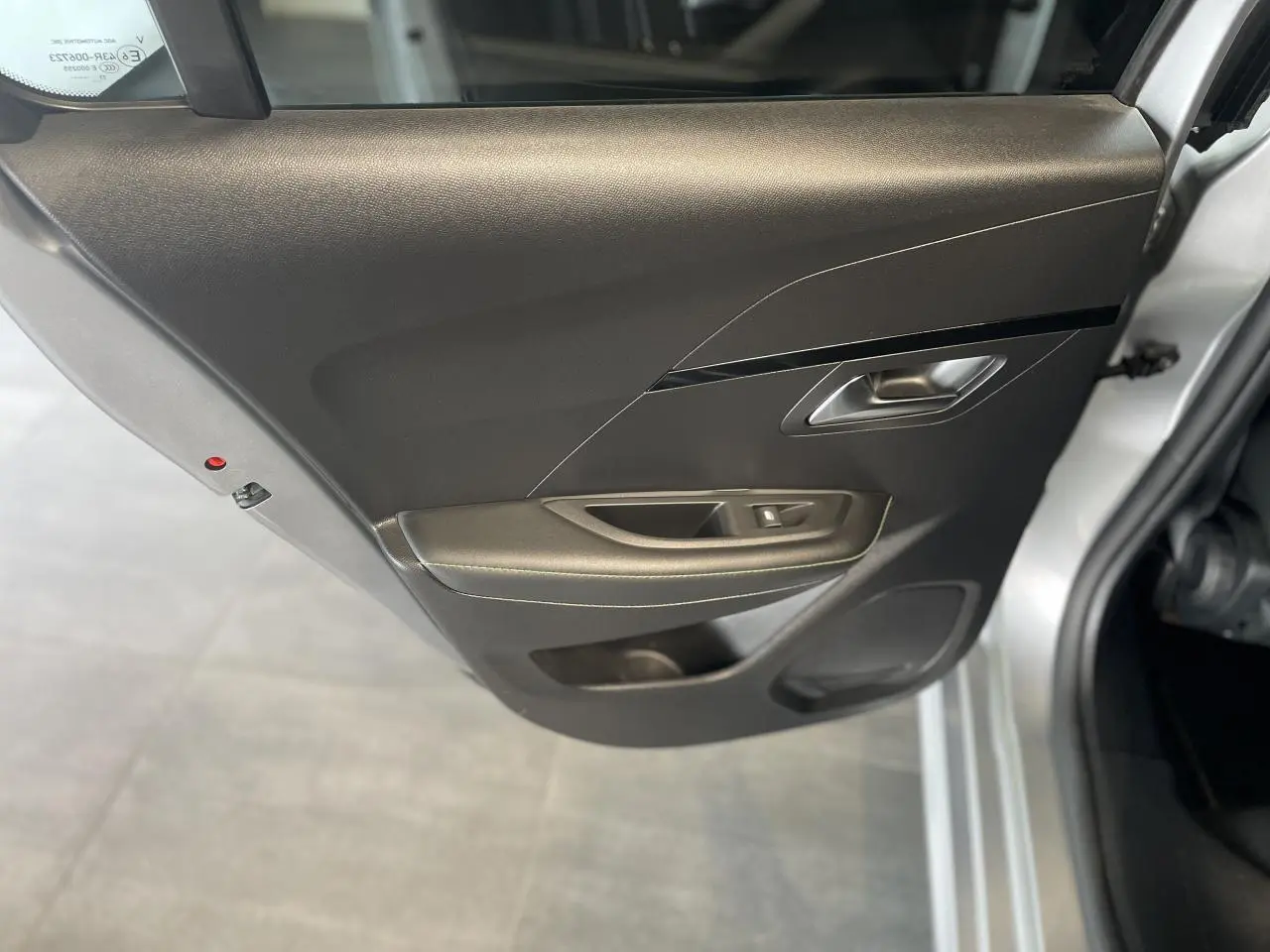 Vue rapprochée de la porte arrière gauche noire avec poignée argentée d'une Peugeot 208 gris clair métallisé.