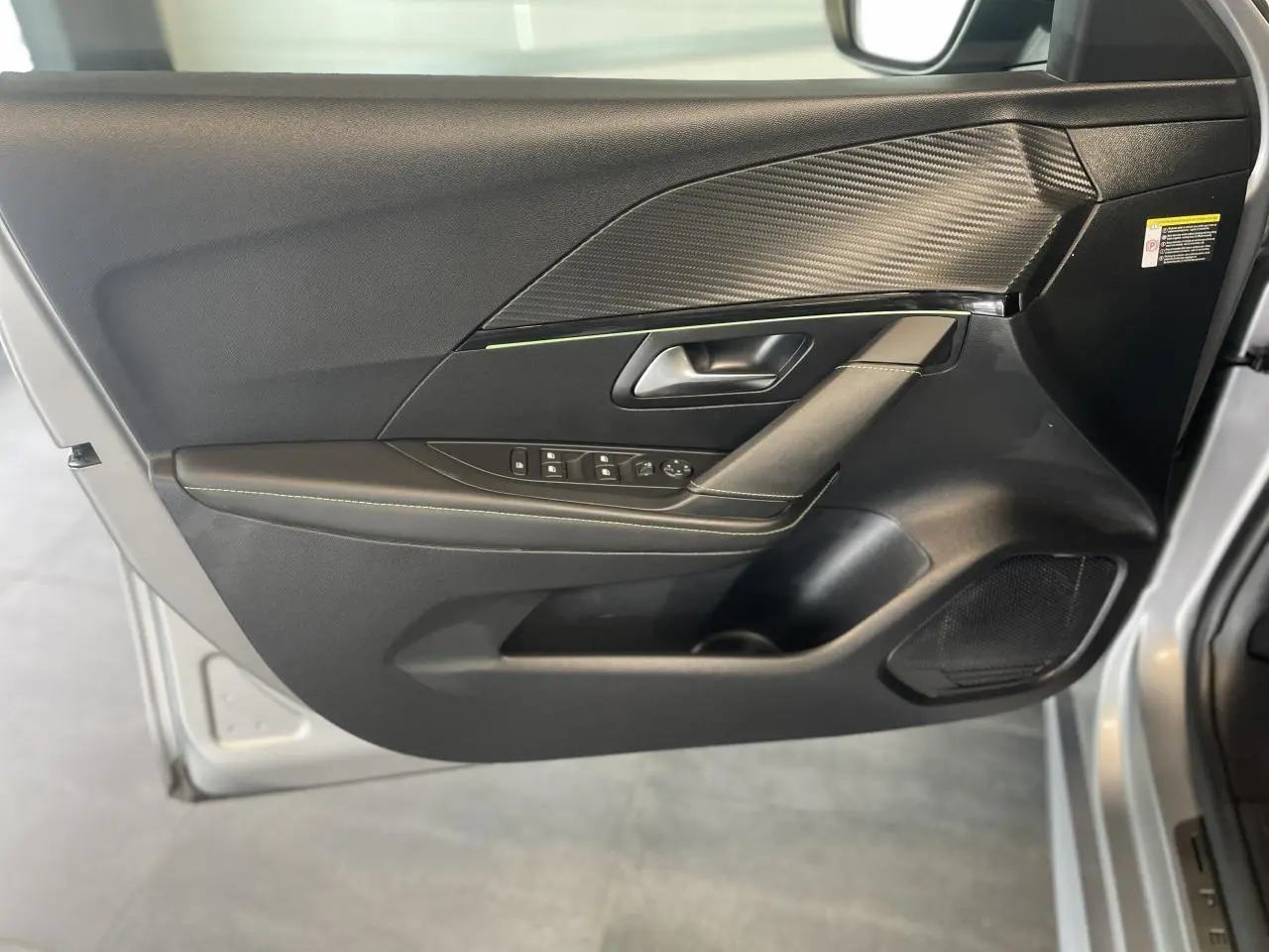 Intérieur côté gauche de la porte PEUGEOT 208 gris clair, avec garniture noire et surpiqûres vertes visibles.