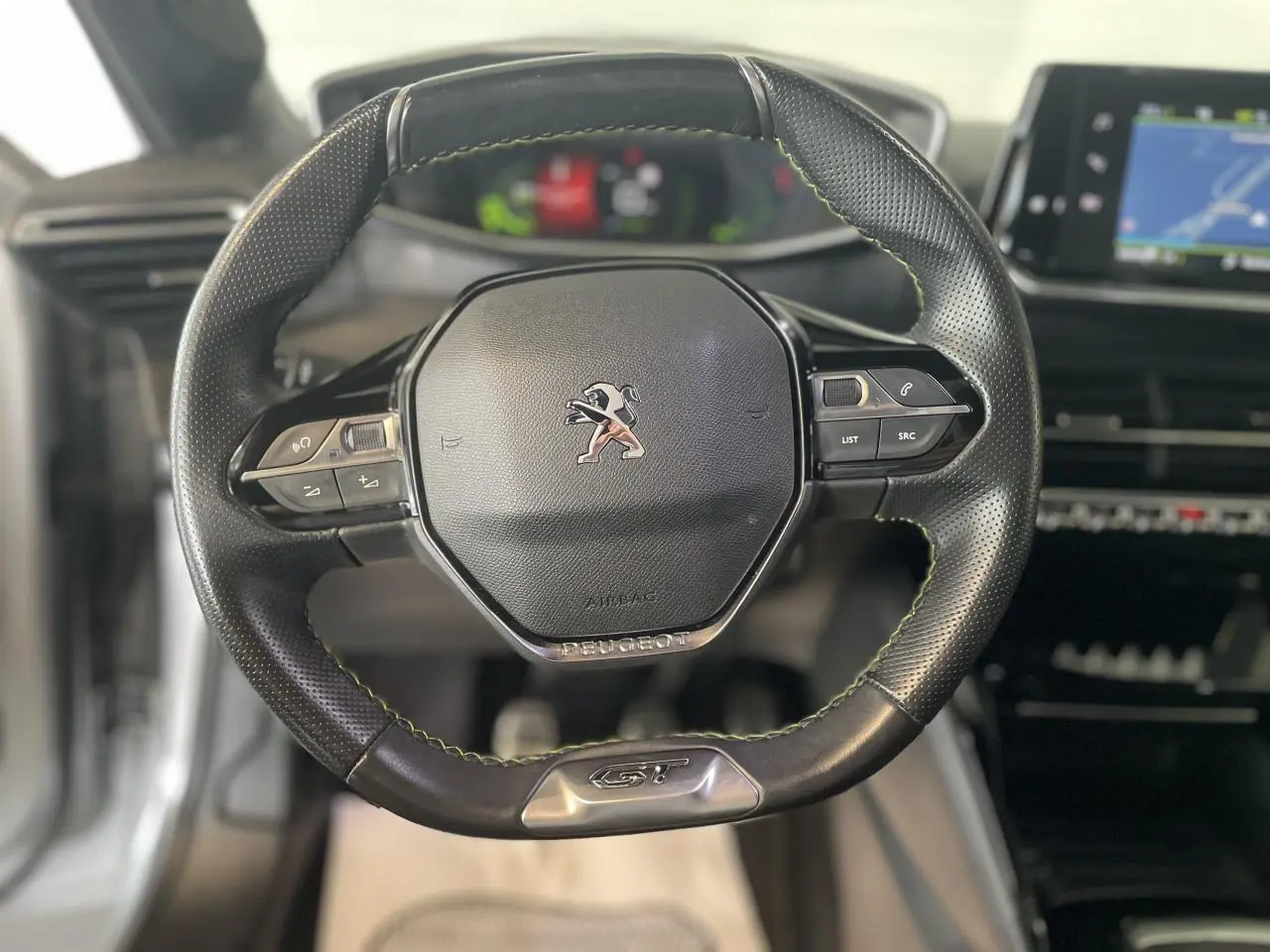 Volant compact cuir noir avec surpiqûres vertes et badge GT au centre du Peugeot 208 gris clair Metal Artense 2023.