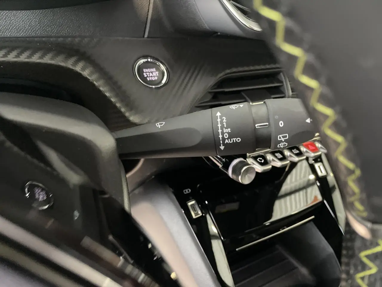 Détail intérieur du Peugeot 208 2023 montrant la commande essuie-glace, bouton start/stop et partie du volant avec surpiqûres vertes.
