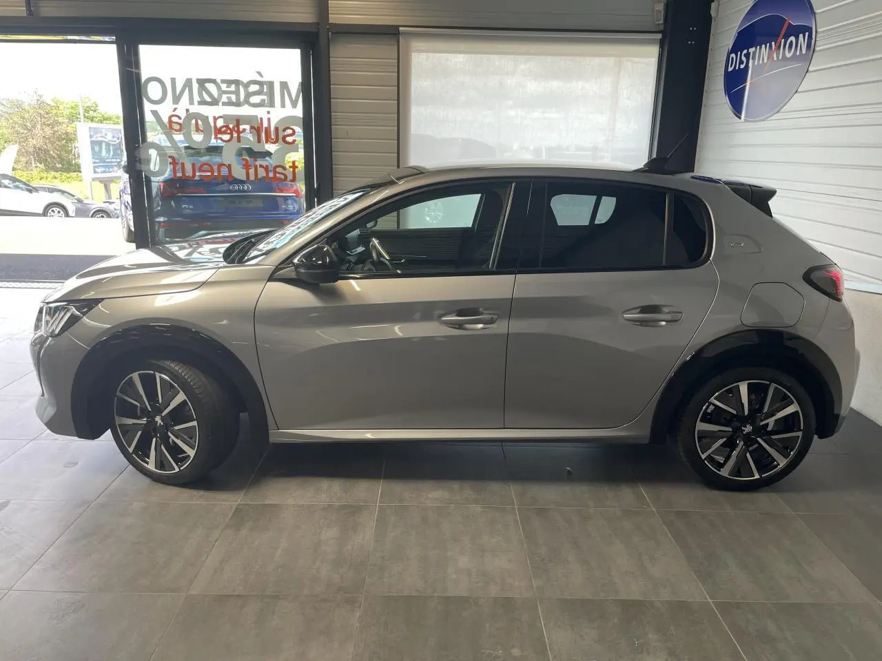 Profil côté gauche d'une Peugeot 208 gris clair métallisé avec toit noir et jantes alliage 17 pouces en showroom.