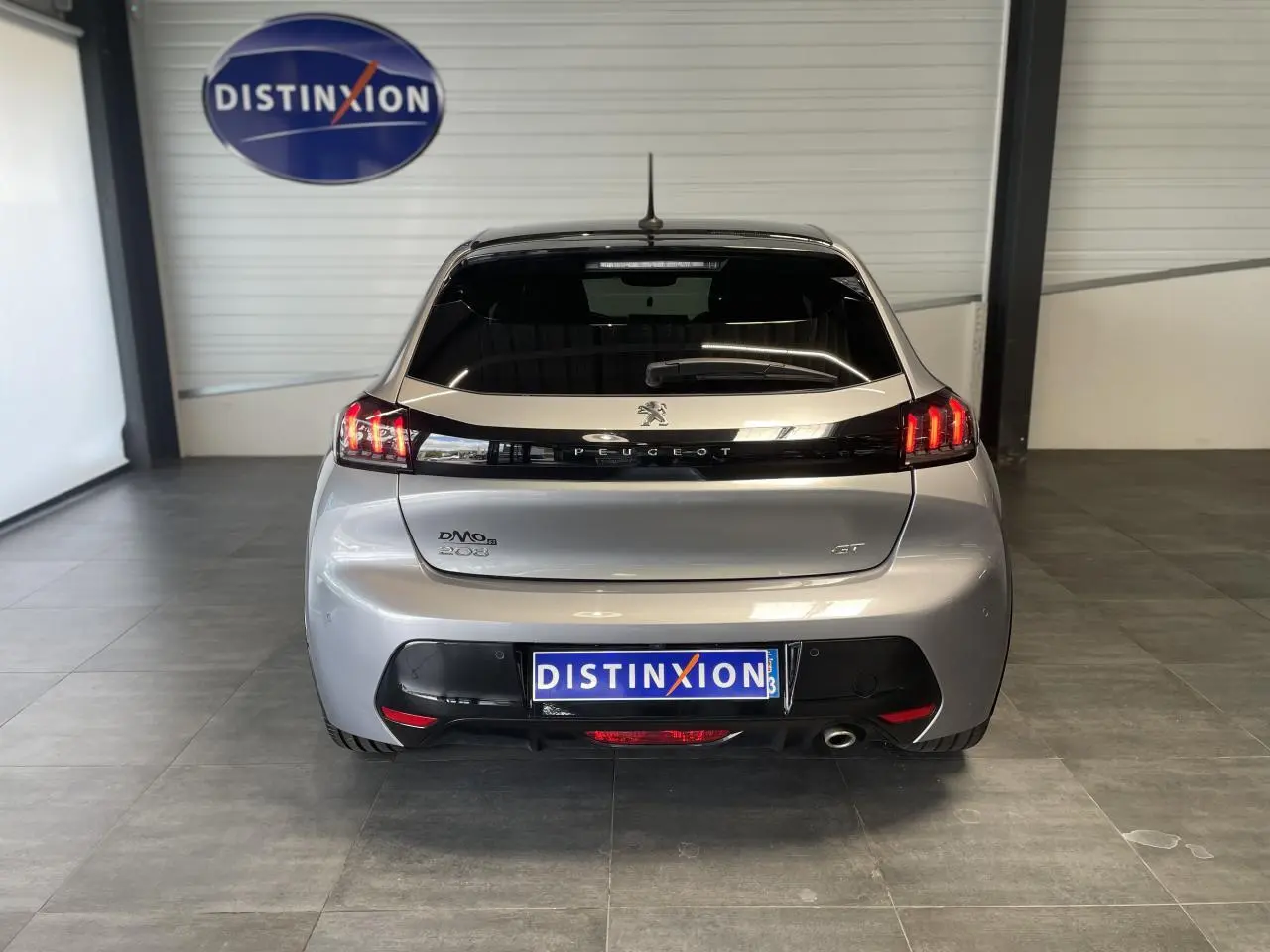 Vue arrière d'une Peugeot 208 gris clair métallisé avec toit noir et feux arrière LED en intérieur showroom.