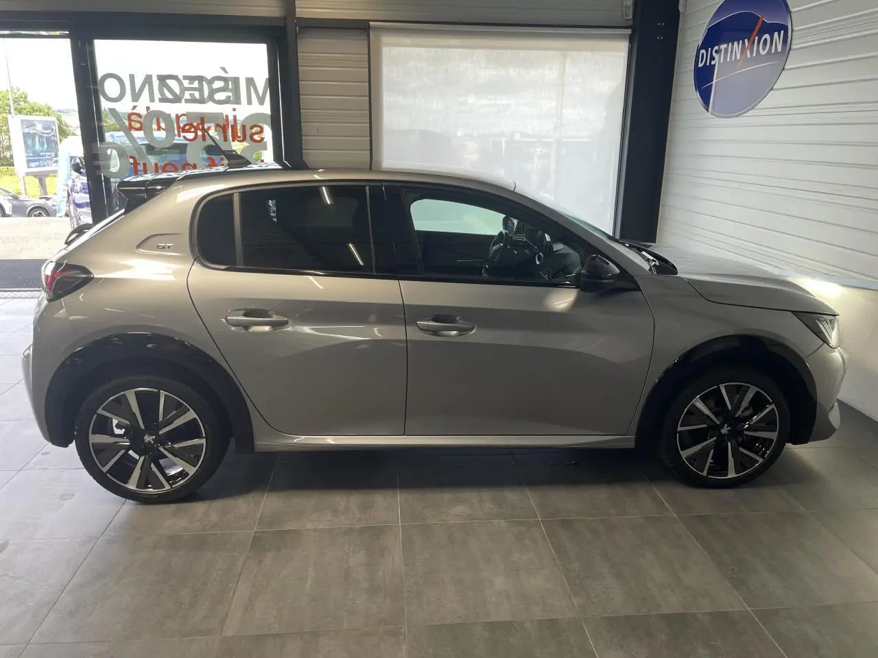 Profil droit d'une Peugeot 208 gris clair Metal Artense avec toit noir et jantes alliage 17'' Bronx en showroom.