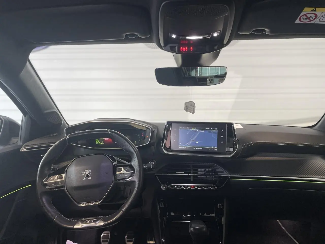 Vue intérieure avant de la Peugeot 208 GT 2023 avec tableau de bord noir, volant compact et écran tactile de navigation.