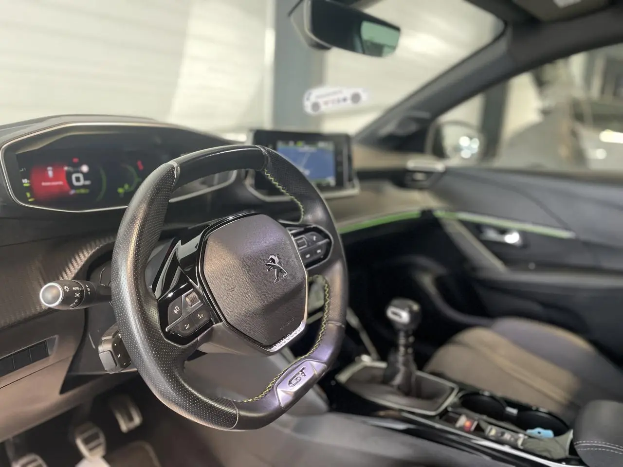 Intérieur Peugeot 208 GT 2023 vu côté conducteur, volant cuir noir avec surpiqûres vertes et tableau de bord numérique.