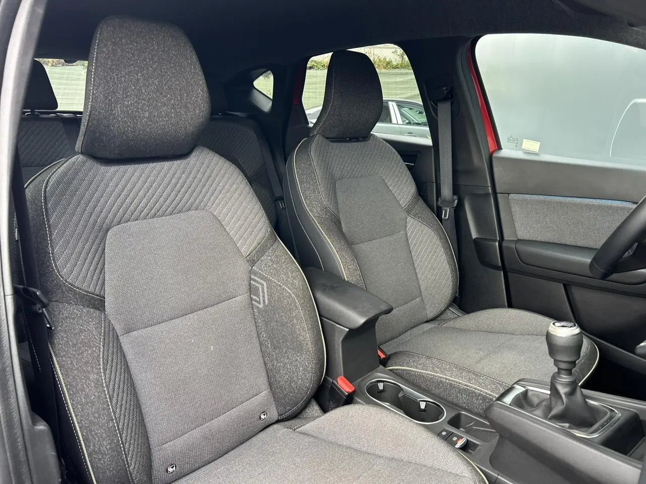 Vue intérieure sur les sièges avant gris avec surpiqûres, accoudoir central et levier de vitesse manuel du Renault Captur rouge.