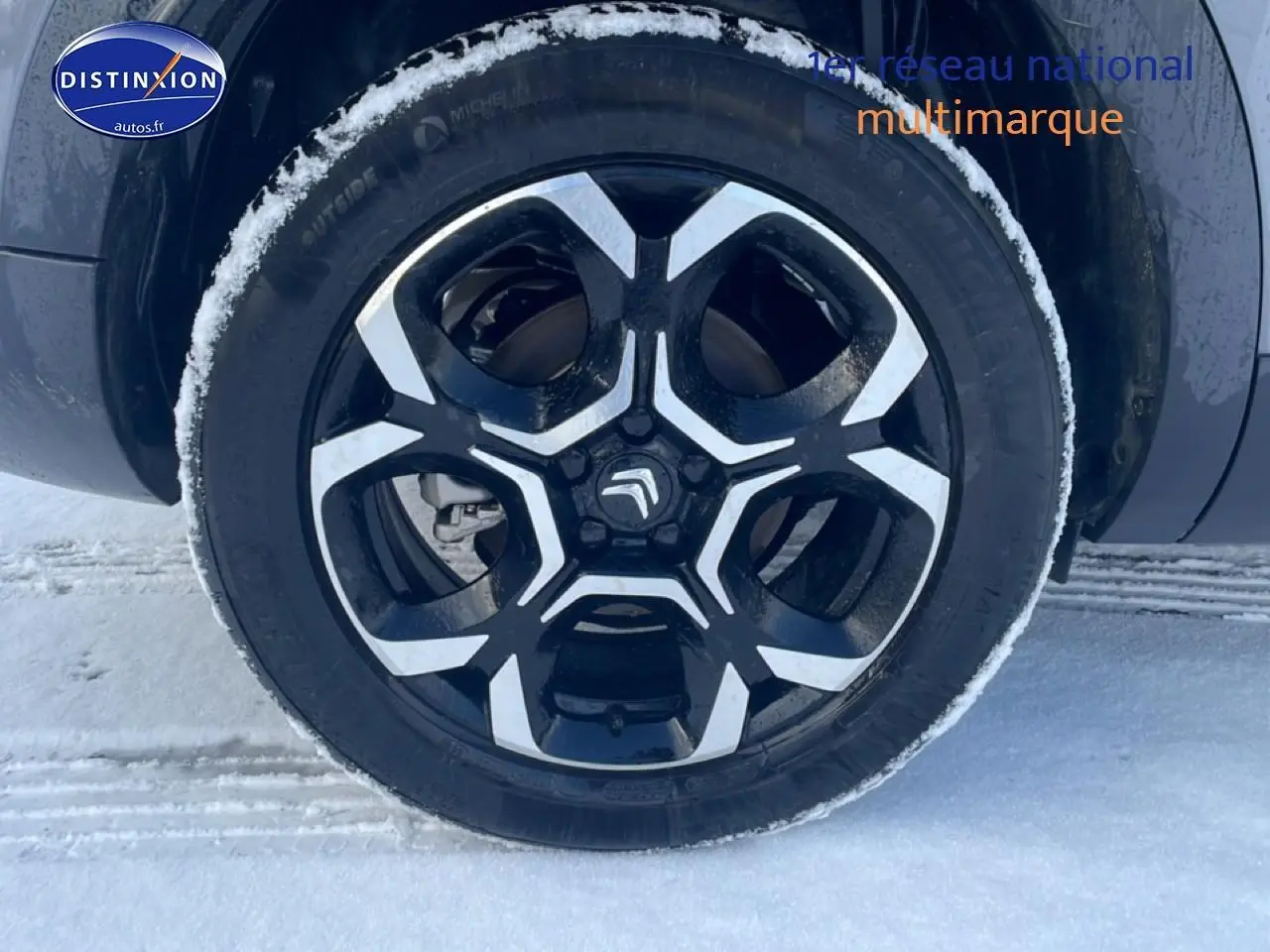 Gros plan sur la jante alu noire et argentée d’un Citroën C5 Aircross gris platinium, avec neige autour du pneu.