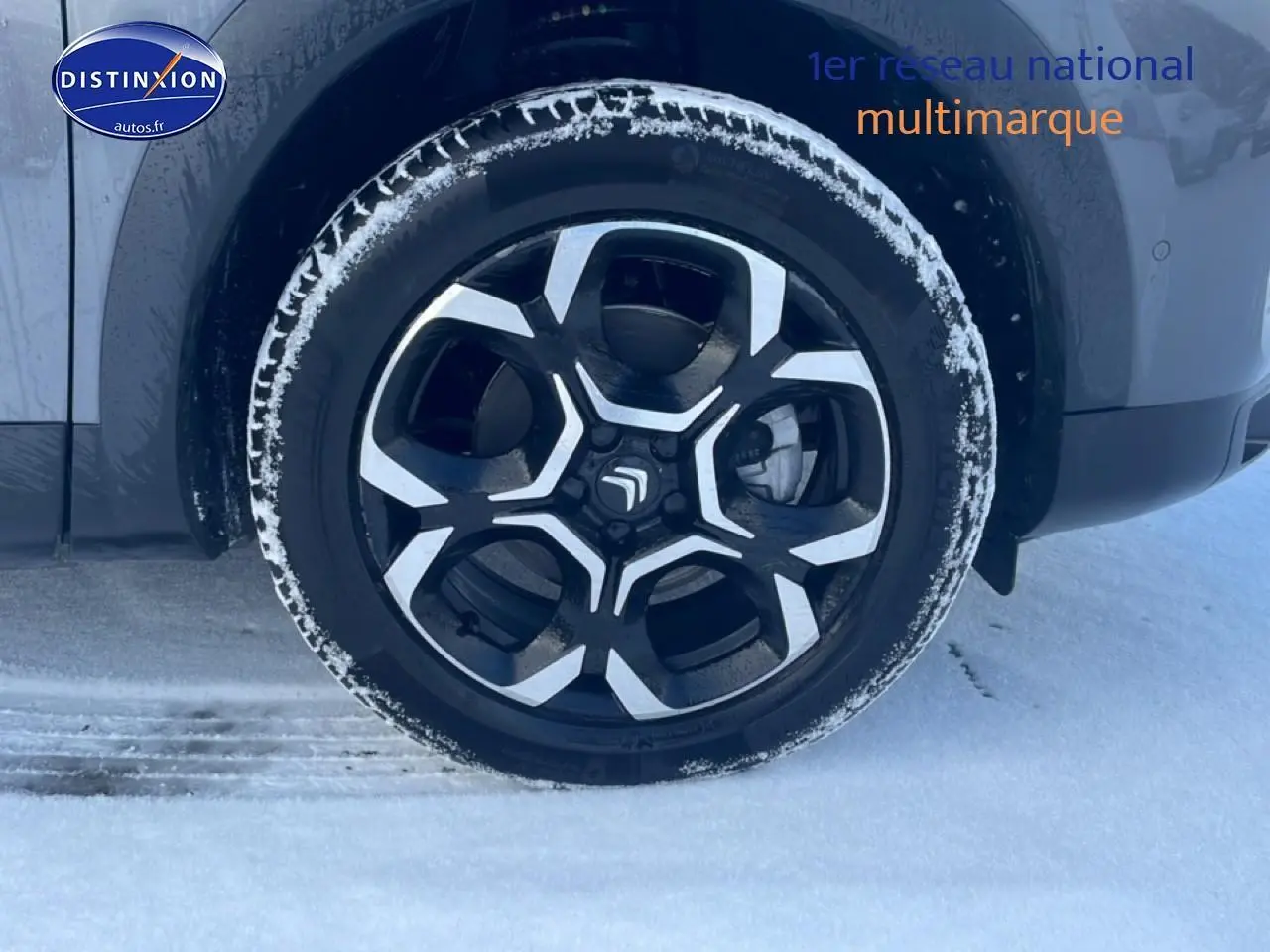 Gros plan sur la roue avant droite du Citroën C5 Aircross gris platinium avec jante alu noire et argentée, neige au sol.