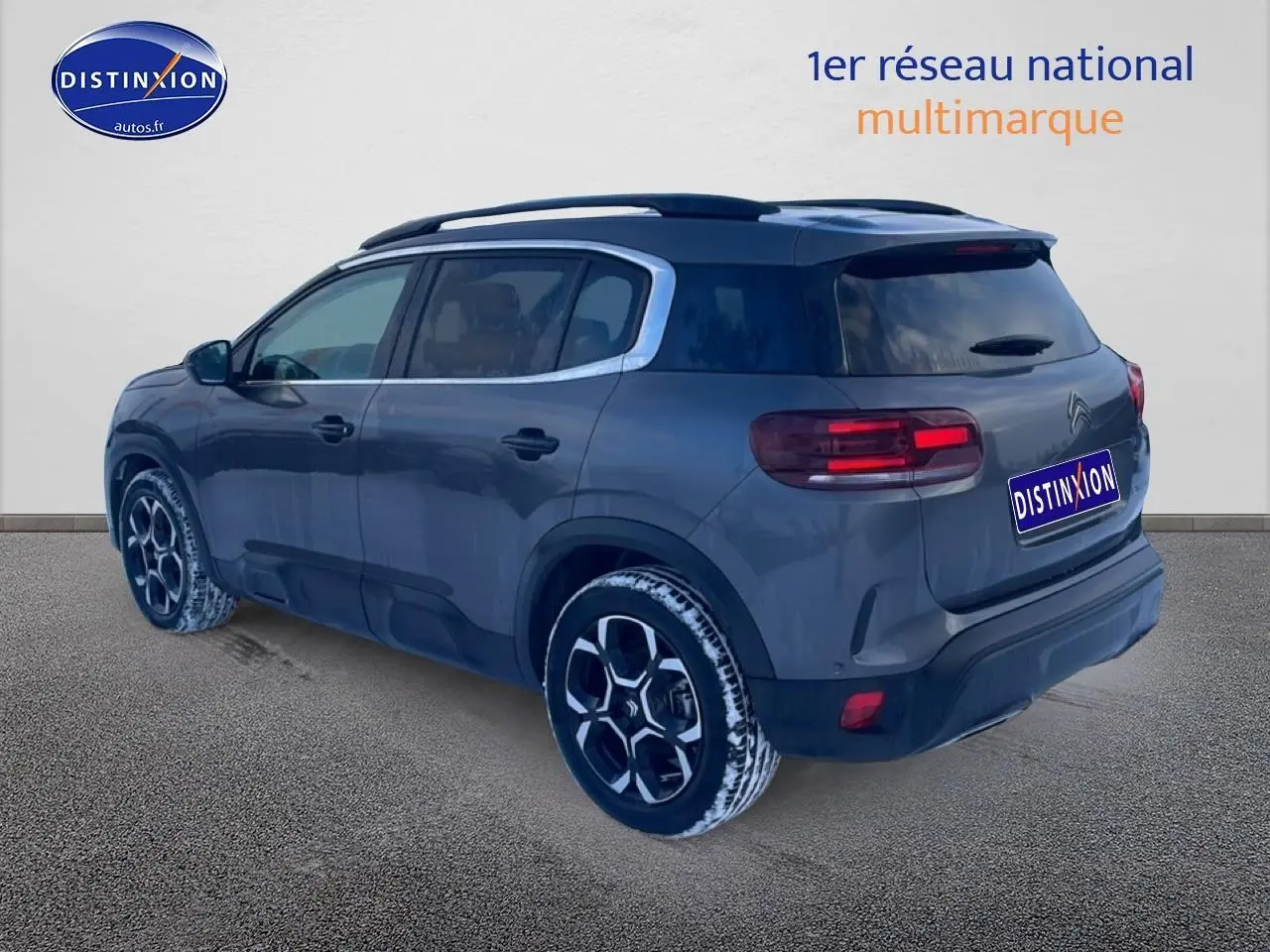 Vue 3/4 arrière droite du Citroën C5 Aircross gris platinium avec jantes alu et barres de toit visibles.