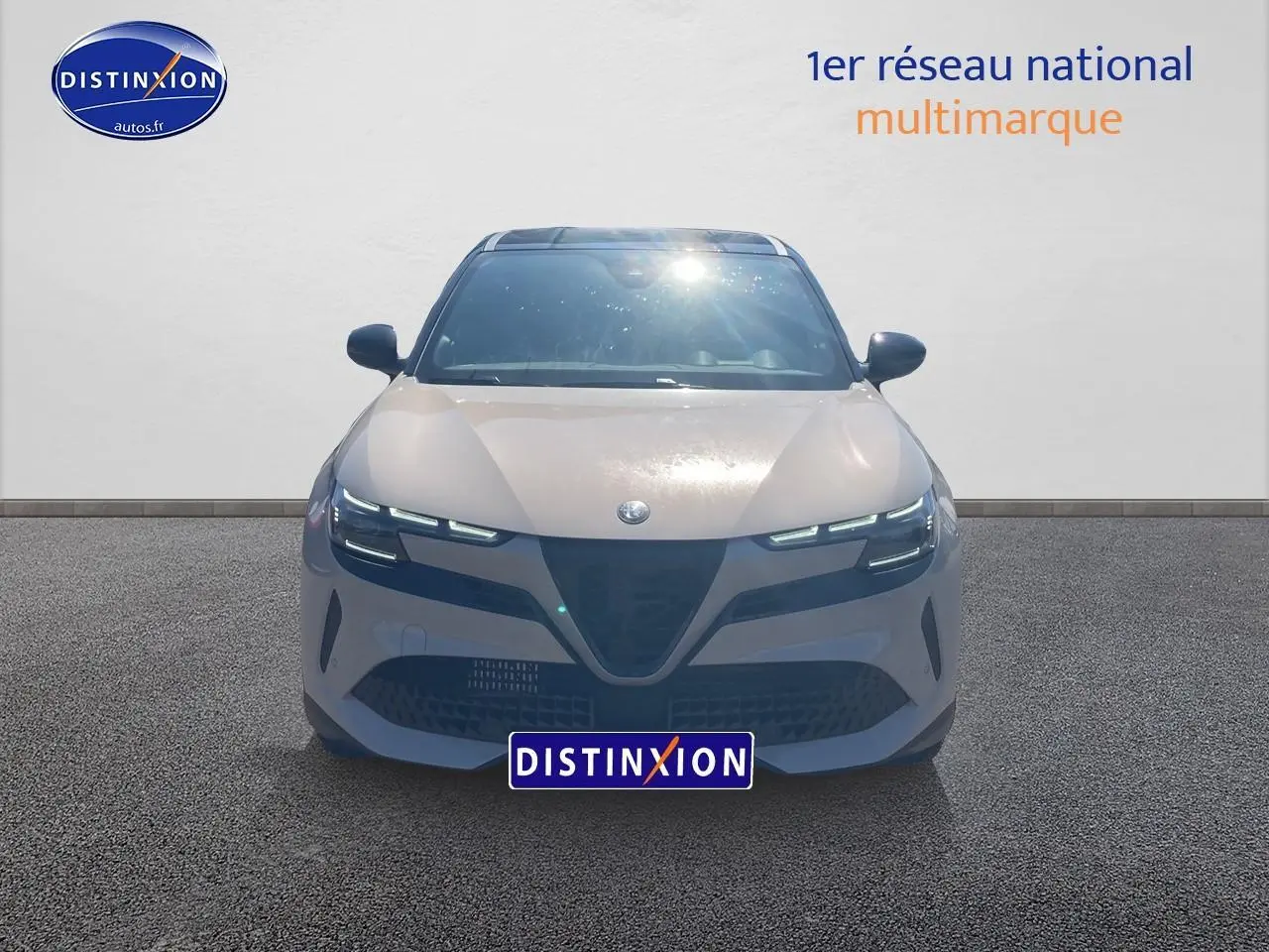 Vue frontale d'une Alfa Romeo Junior 1.2 hybride ivoire et noir avec phares matrix LED allumés sur fond neutre.