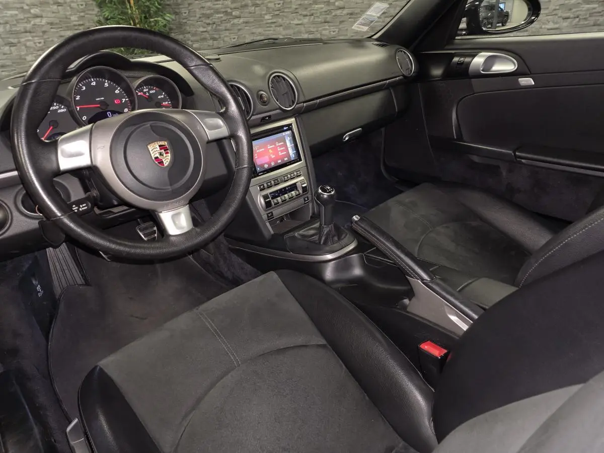 Intérieur noir de Porsche Cayman 2.7i 2008 vu côté conducteur, volant cuir et console centrale avec boîte manuelle.