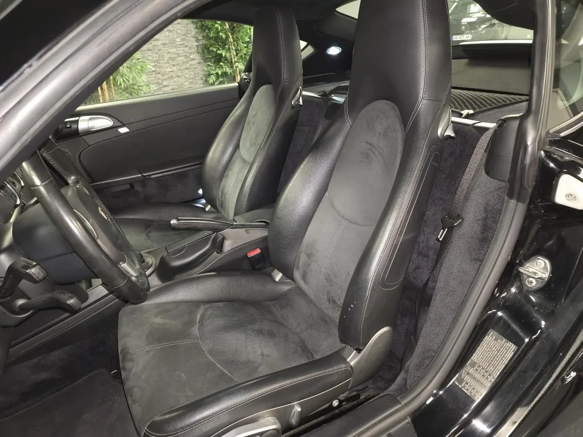Vue intérieure côté gauche de la Porsche Cayman 2.7i noire de 2008, avec sièges sport en cuir et alcantara.