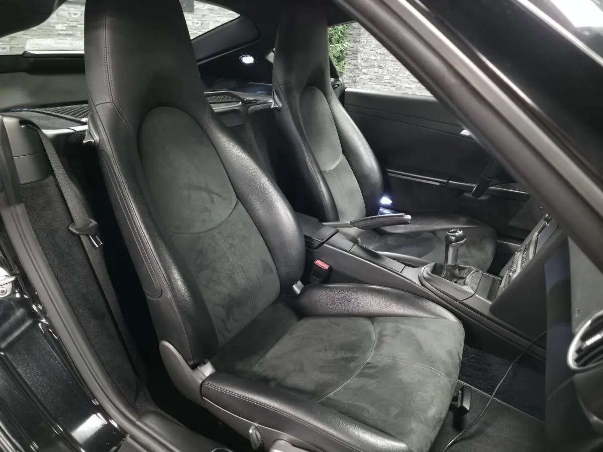 Vue intérieure côté droit de la Porsche Cayman 2.7i noire de 2008, sièges sport en Alcantara et cuir avec levier de vitesses manuel.