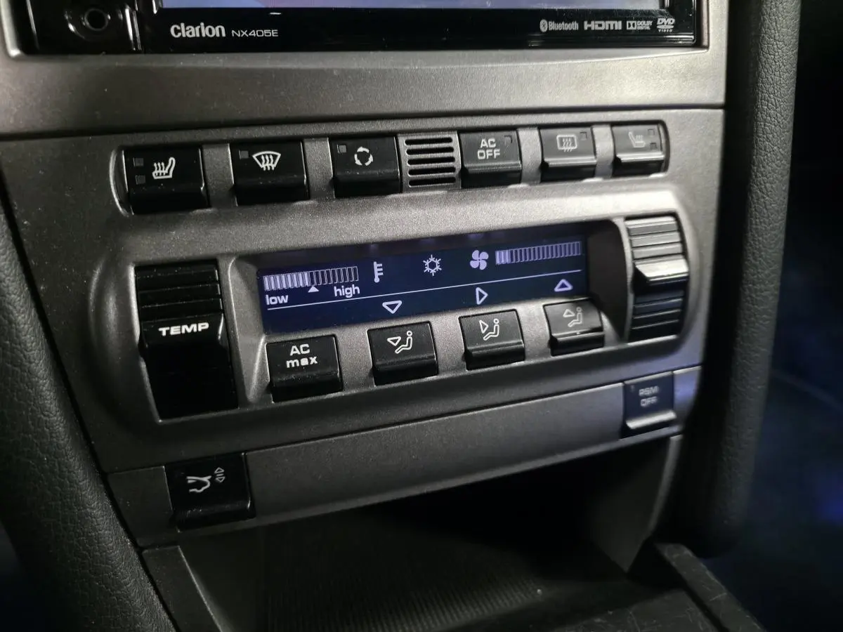 Détail de la console centrale noire de la Porsche Cayman 2.7i 2008 avec commandes climatisation et boutons de réglage.
