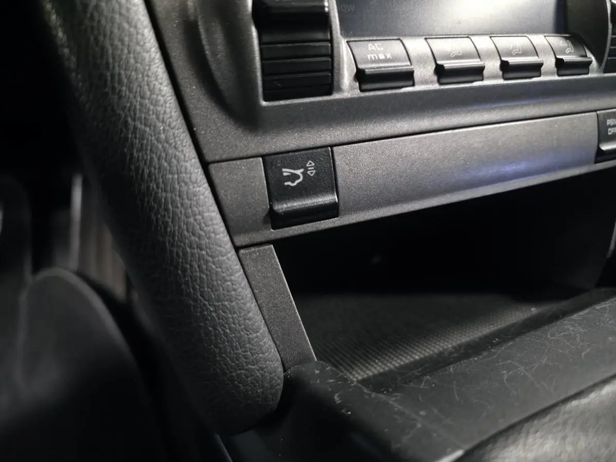 Gros plan sur la console centrale noire de la Porsche Cayman 2.7i 2008, montrant les boutons de commande et un rangement ouvert.