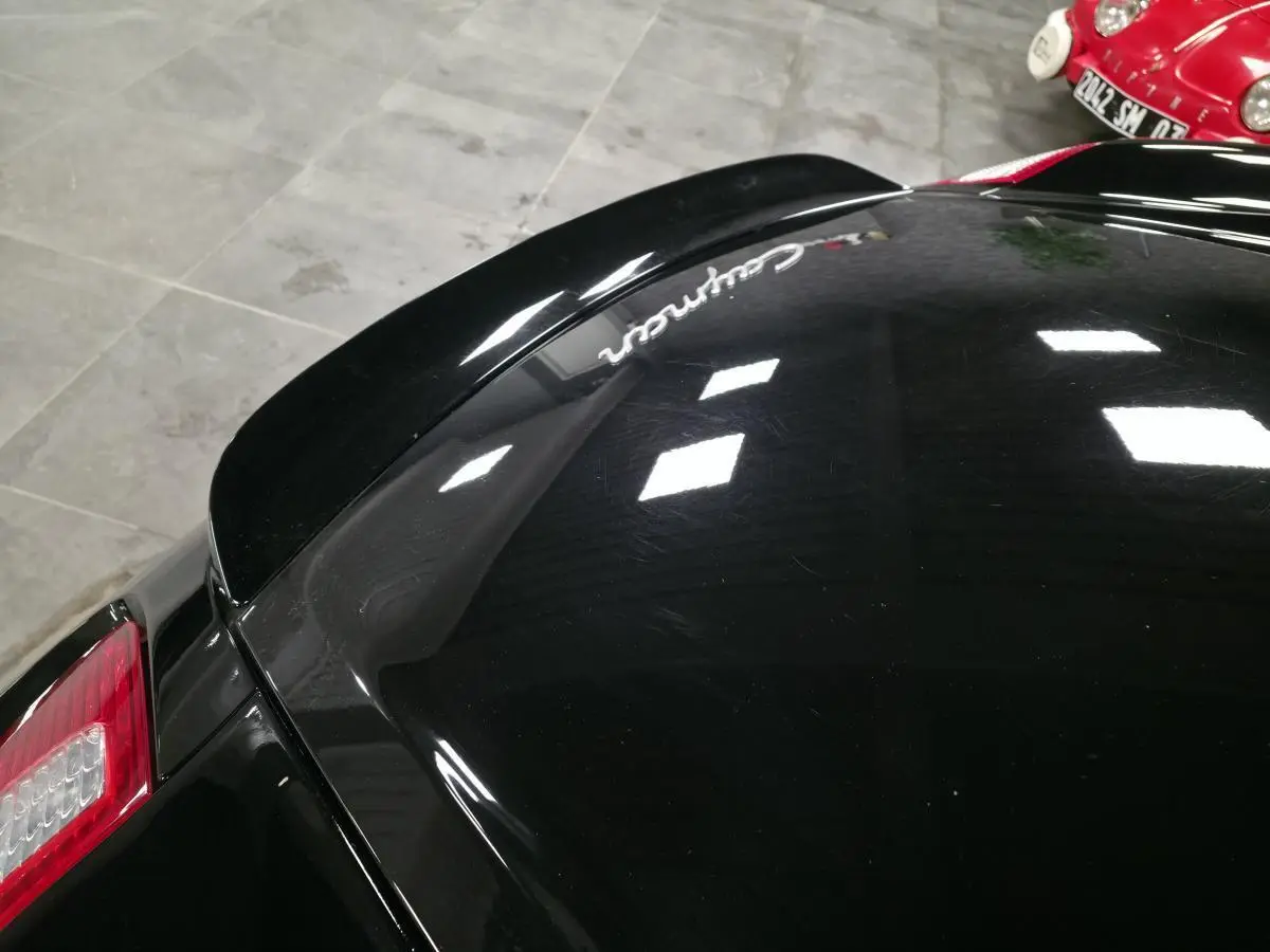 Vue rapprochée arrière gauche d’une Porsche Cayman 2.7i noire avec aileron arrière déployé et feu arrière rouge.