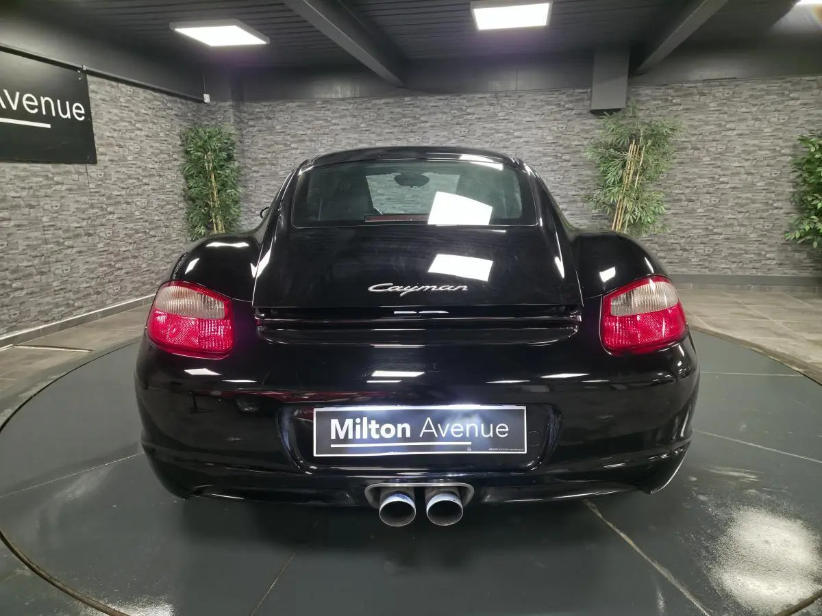Vue arrière d'une Porsche Cayman 2.7i noire de 2008 avec double sortie d'échappement centrale et feux rouges.