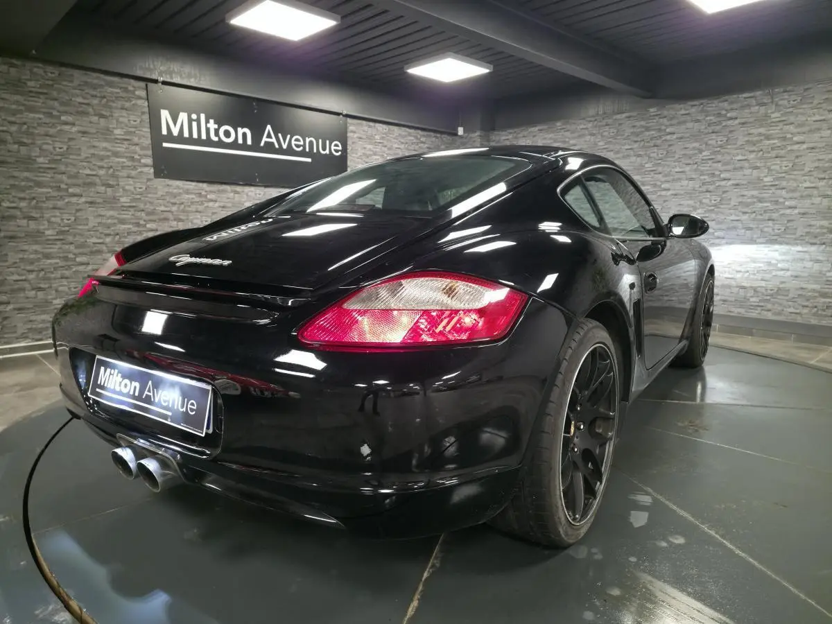 Vue 3/4 arrière droite d'une Porsche Cayman 2.7i noire avec jantes SportDesign noires et double sortie d'échappement centrale.