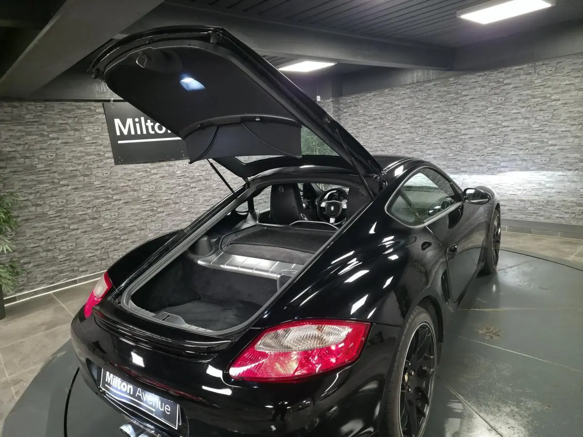 Vue 3/4 arrière droite d'une Porsche Cayman 2.7i noire avec coffre arrière ouvert et jantes SportDesign noires.