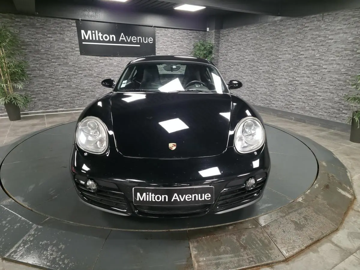 Vue avant d'une Porsche Cayman 2.7i noire, avec phares bi-xénon et plaque Milton Avenue visible.