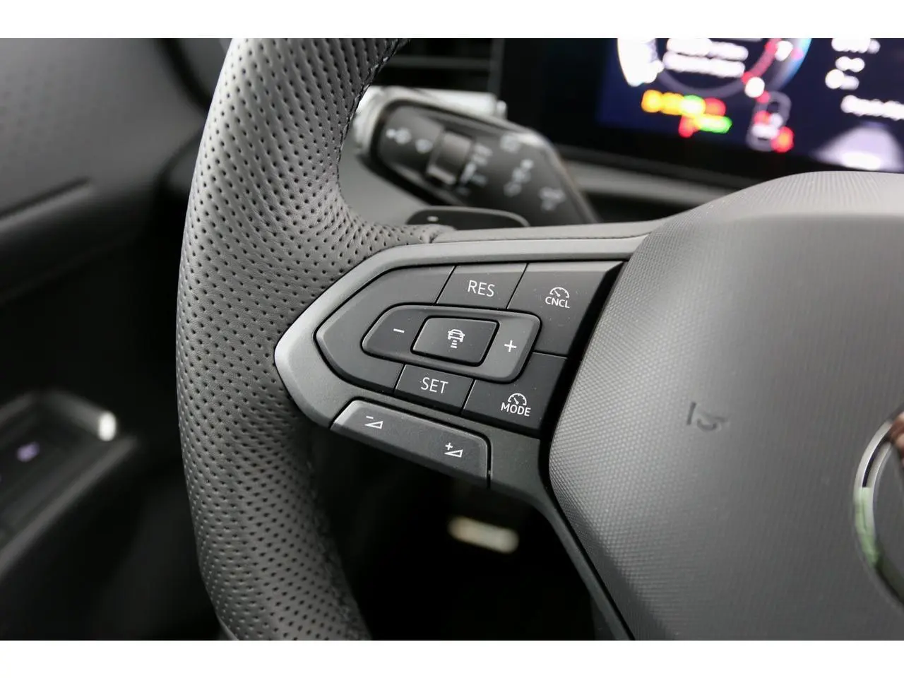 Gros plan sur les commandes gauche du volant perforé du Volkswagen T-Roc 2026, intérieur noir avec affichage numérique flou.