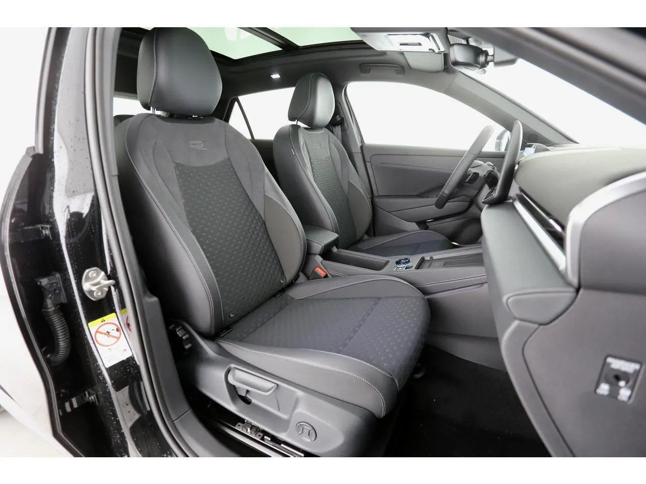 Vue intérieure côté gauche du Volkswagen T-Roc 2026, sièges sport R-Line en tissu noir avec surpiqûres grises.