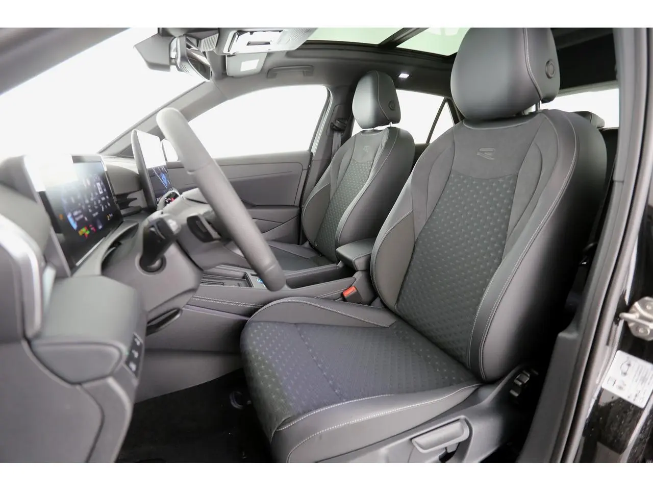 Vue intérieure côté conducteur du Volkswagen T-Roc 2026, sièges sport R-Line en tissu noir avec surpiqûres grises.