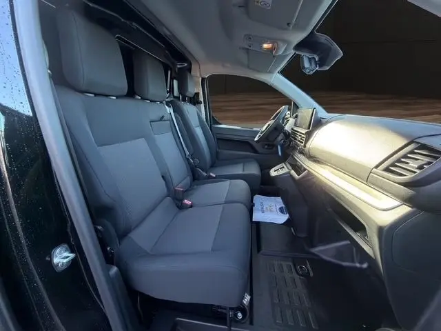 Vue intérieure côté conducteur du Peugeot Expert Fourgon noir, montrant les sièges avant et le tableau de bord moderne.