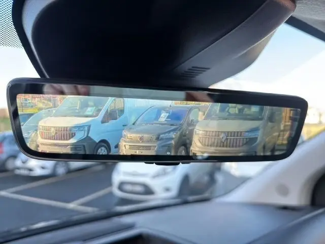 Vue dans le rétroviseur intérieur montrant un Peugeot Expert Fourgon noir garé parmi d'autres véhicules utilitaires.