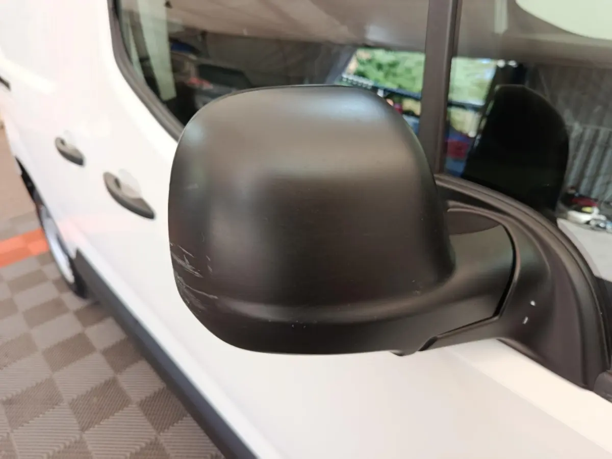 Gros plan sur le rétroviseur noir côté droit d’un Peugeot Partner blanc vu de profil avant.