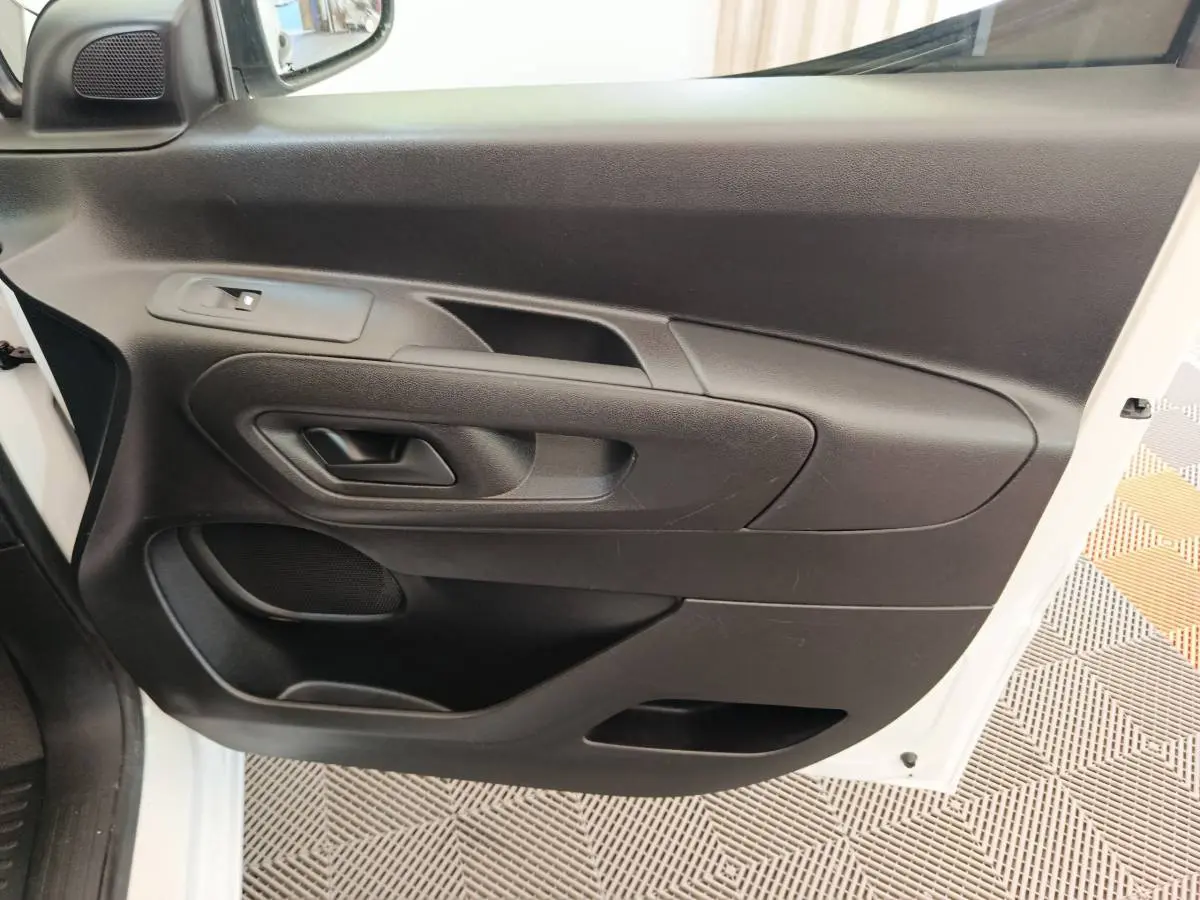 Vue rapprochée de la porte avant gauche noire du Peugeot Partner blanc, avec poignée et haut-parleur intégrés.