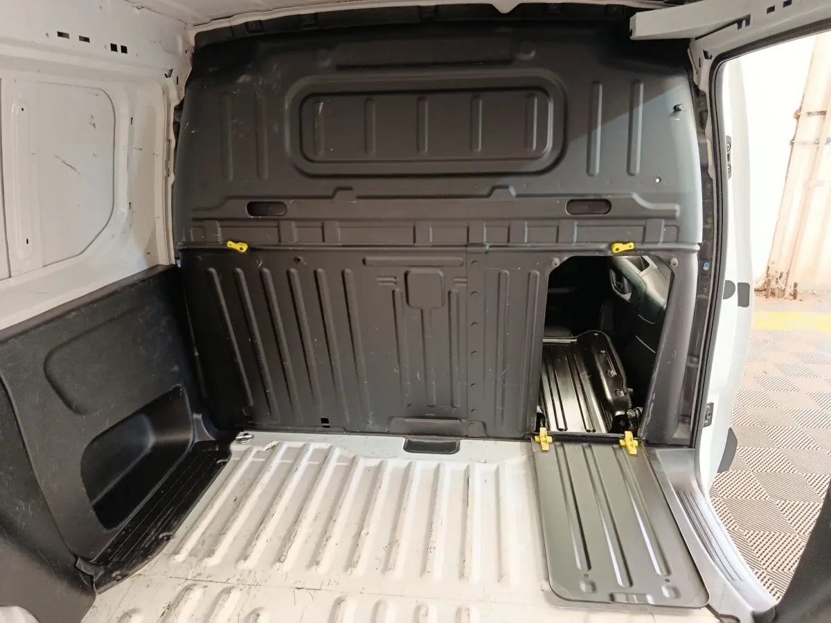 Vue intérieure du compartiment de chargement blanc du Peugeot Partner avec cloison pleine noire et trappe d'accès ouverte côté droit.