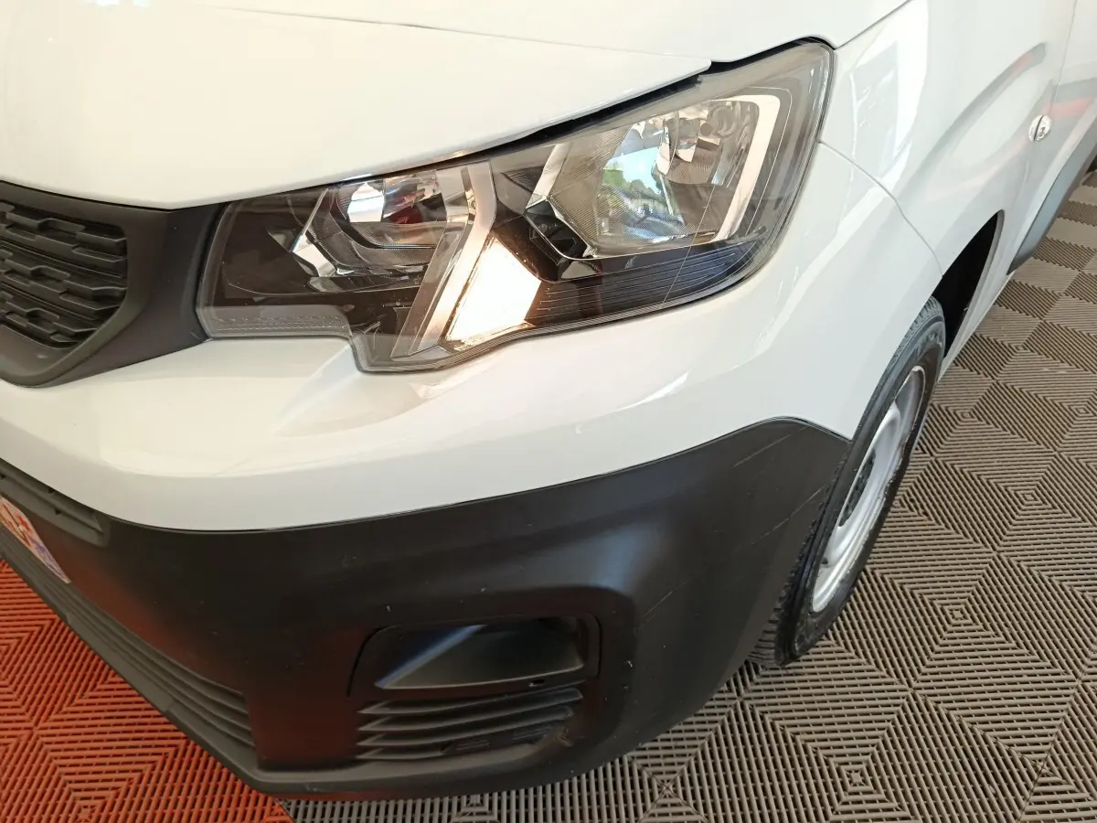 Vue rapprochée du phare avant droit d’un Peugeot Partner blanc avec pare-chocs noir et jante acier.