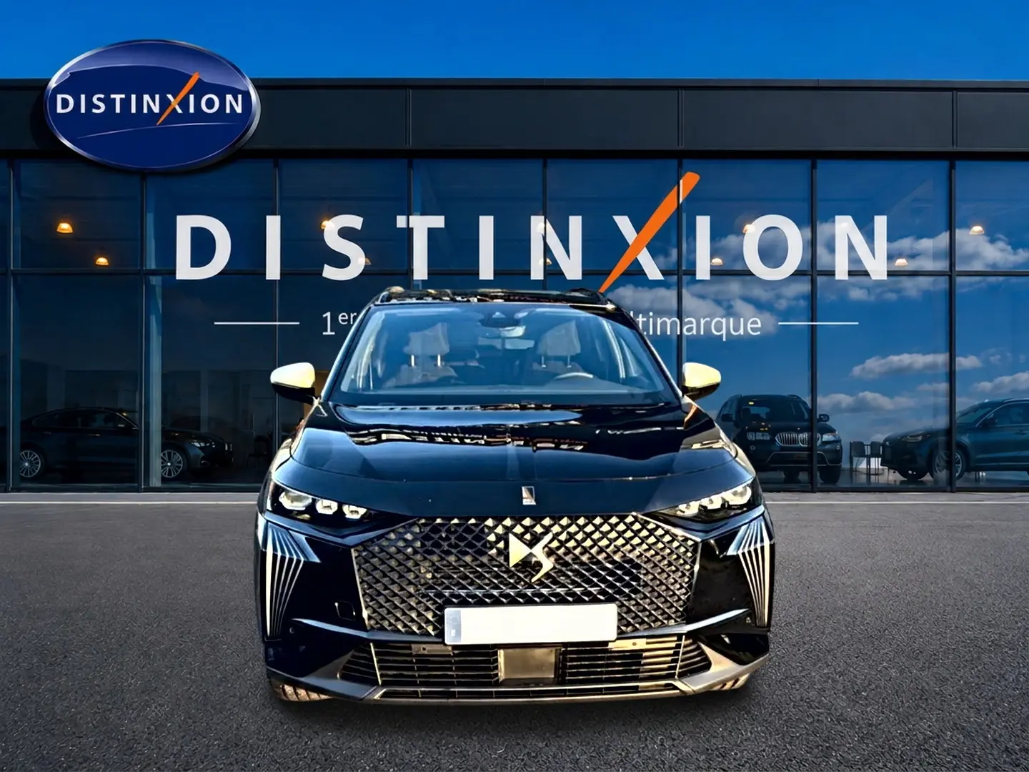 Vue frontale d’un DS7 noir avec calandre distinctive et rétroviseurs blancs devant une vitrine Distinxion.