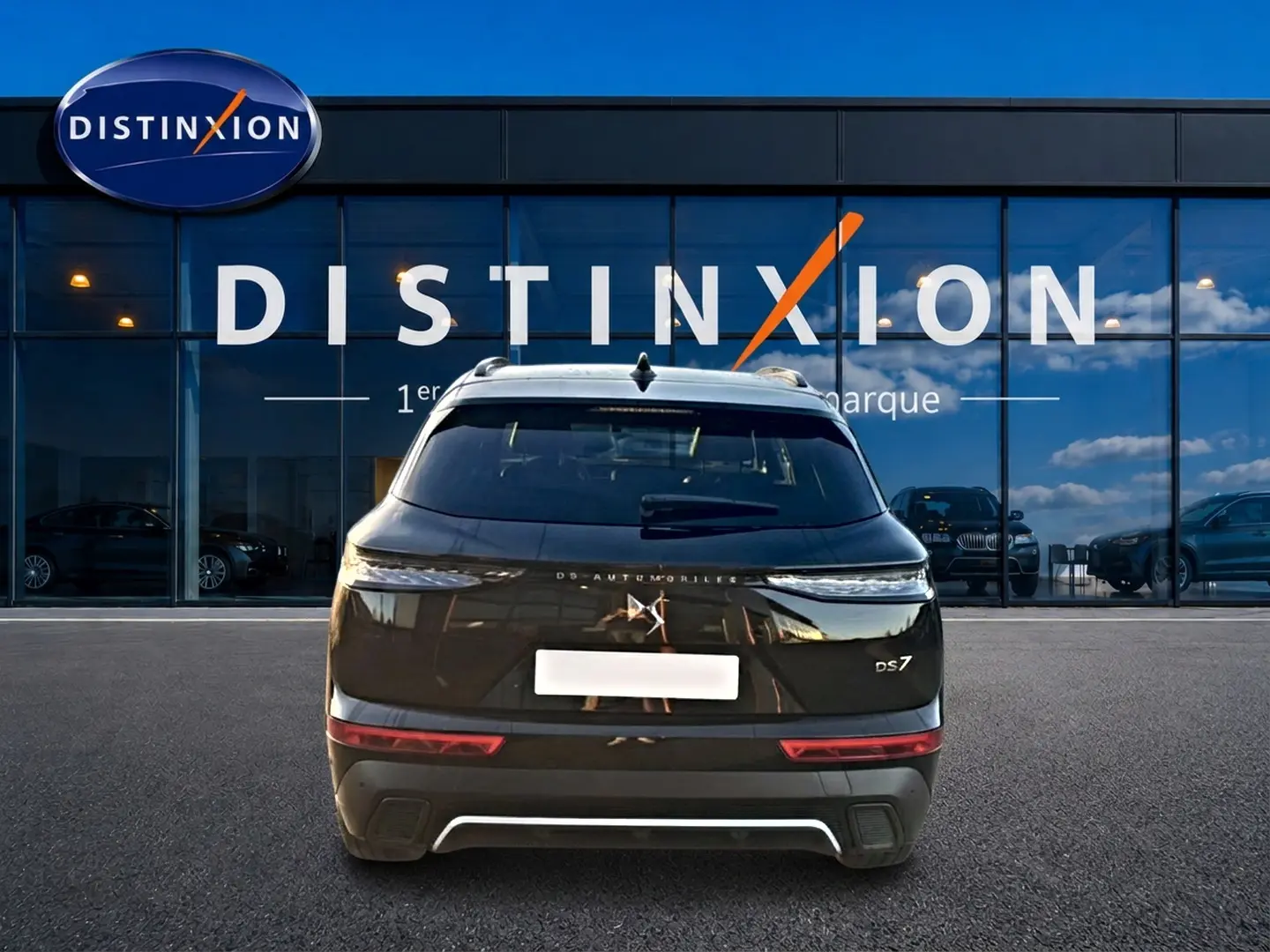 Vue arrière d'un DS7 noir 2026 avec feux LED fins et logo DS distinctif, stationné devant une vitrine Distinxion.