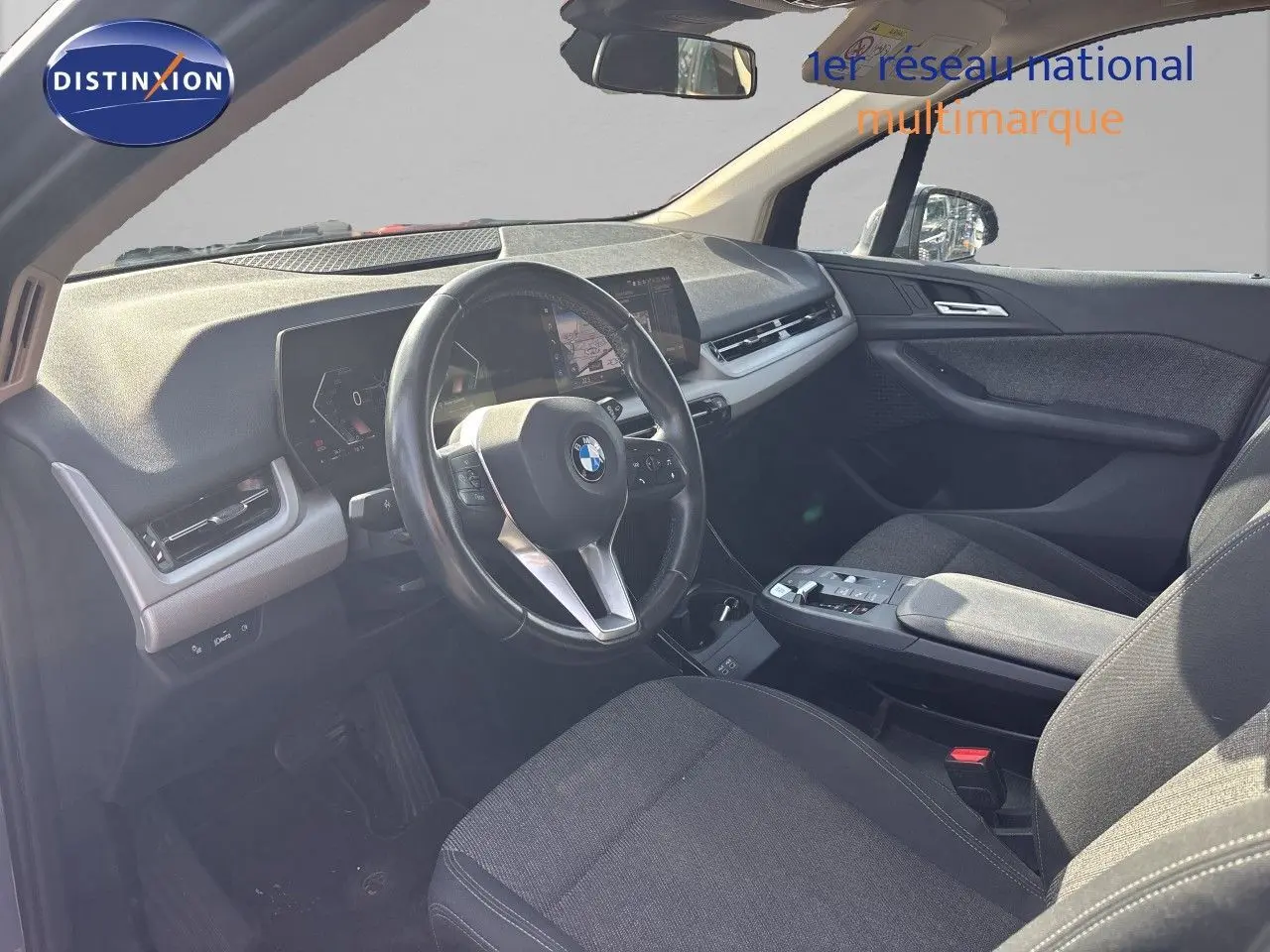Vue intérieure côté conducteur de la BMW Série 2 Active Tourer 218d 2023 avec tableau de bord moderne et sièges tissu gris.