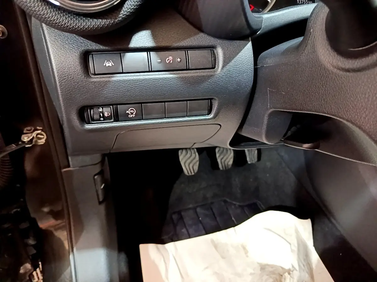 Vue intérieure côté conducteur du tableau de bord noir avec commandes d'assistance et pédales du Nissan Juke 2023.