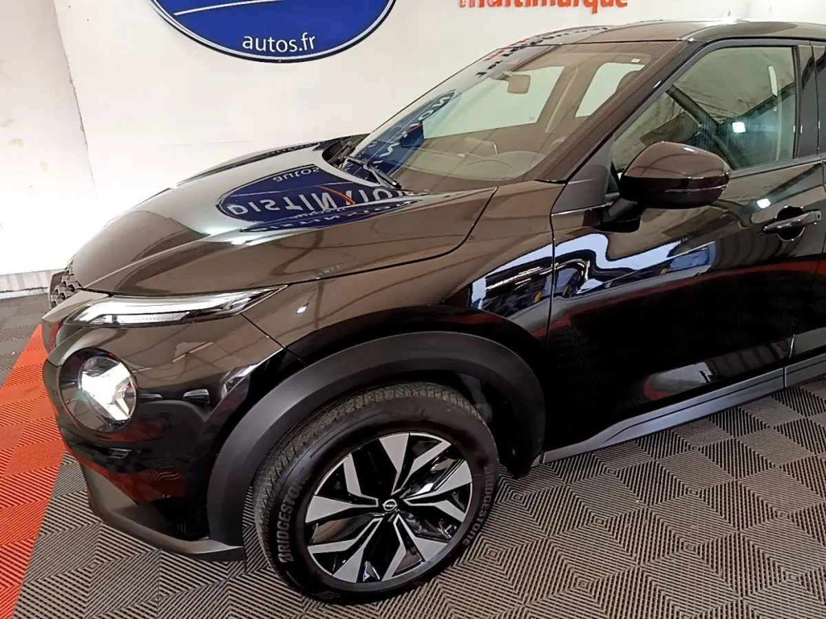 Vue 3/4 avant gauche du Nissan Juke noir 2023 avec jantes alliage bicolores et phares LED ellipsoïdaux.