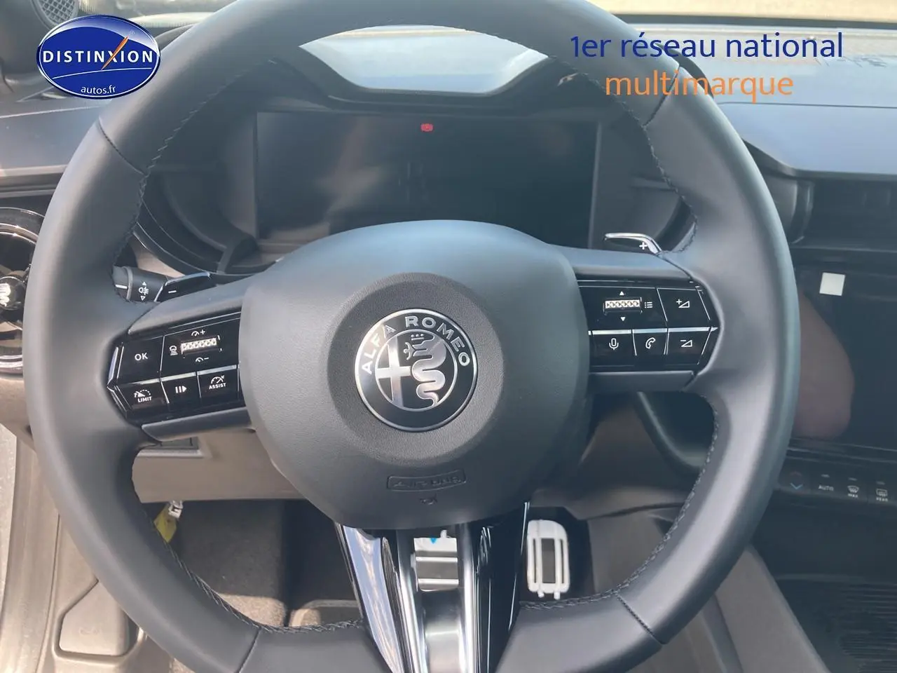 Vue rapprochée du volant noir de l'Alfa Romeo Junior 1.2 hybride avec commandes intégrées et tableau de bord digital.