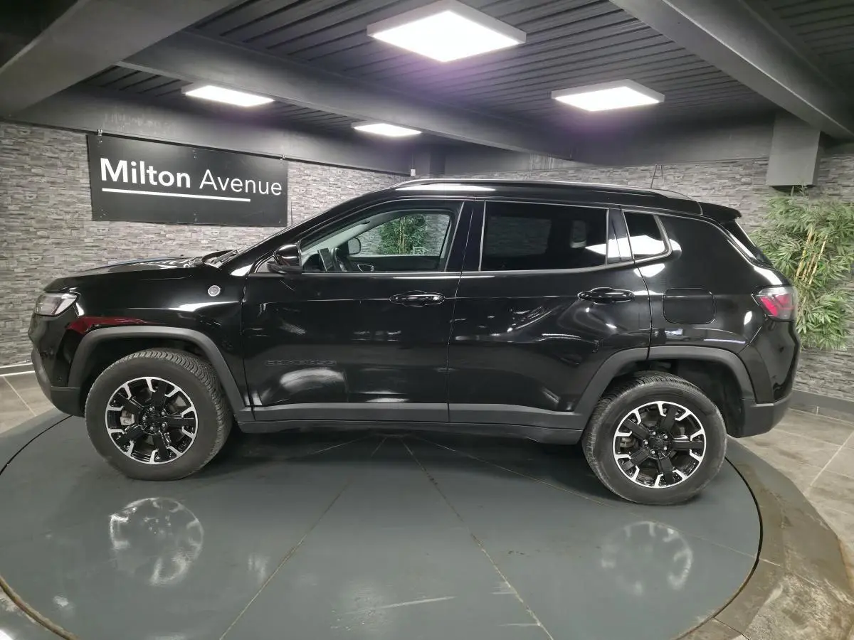 Profil côté gauche d'un Jeep Compass Trailhawk noir brillant, avec jantes alliage noires et toit assorti.
