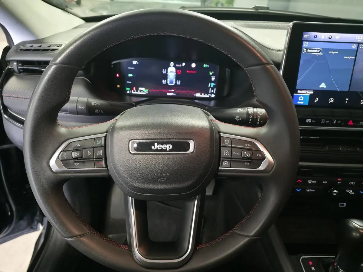 Vue rapprochée du volant noir avec surpiqûres rouges du Jeep Compass 2022, affichage numérique et écran tactile visible.