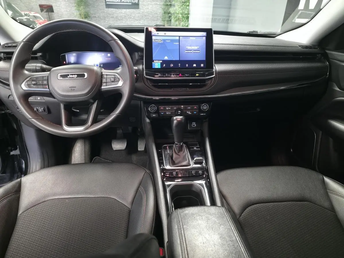 Vue intérieure avant du Jeep Compass Trailhawk 2022, tableau de bord noir avec écran tactile central et volant multifonction.