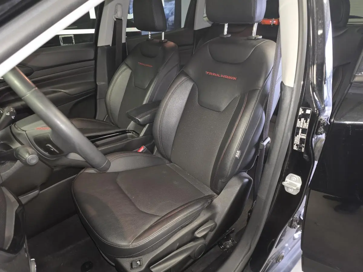 Vue intérieure côté conducteur du Jeep Compass Trailhawk 2022 noir, sièges en cuir noir avec logo Trailhawk rouge brodé.