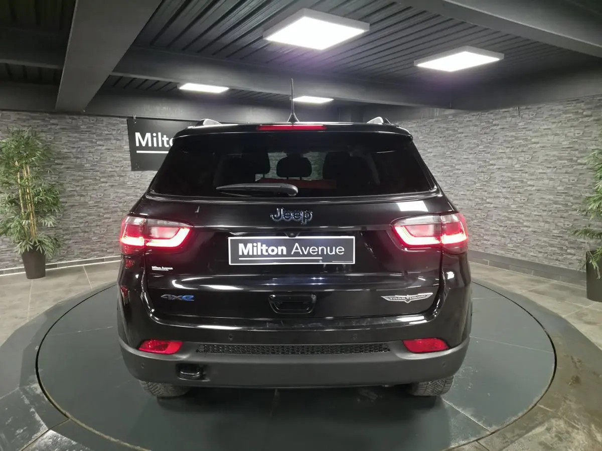 Vue arrière d'un Jeep Compass Trailhawk noir brillant avec feux LED allumés dans un showroom.