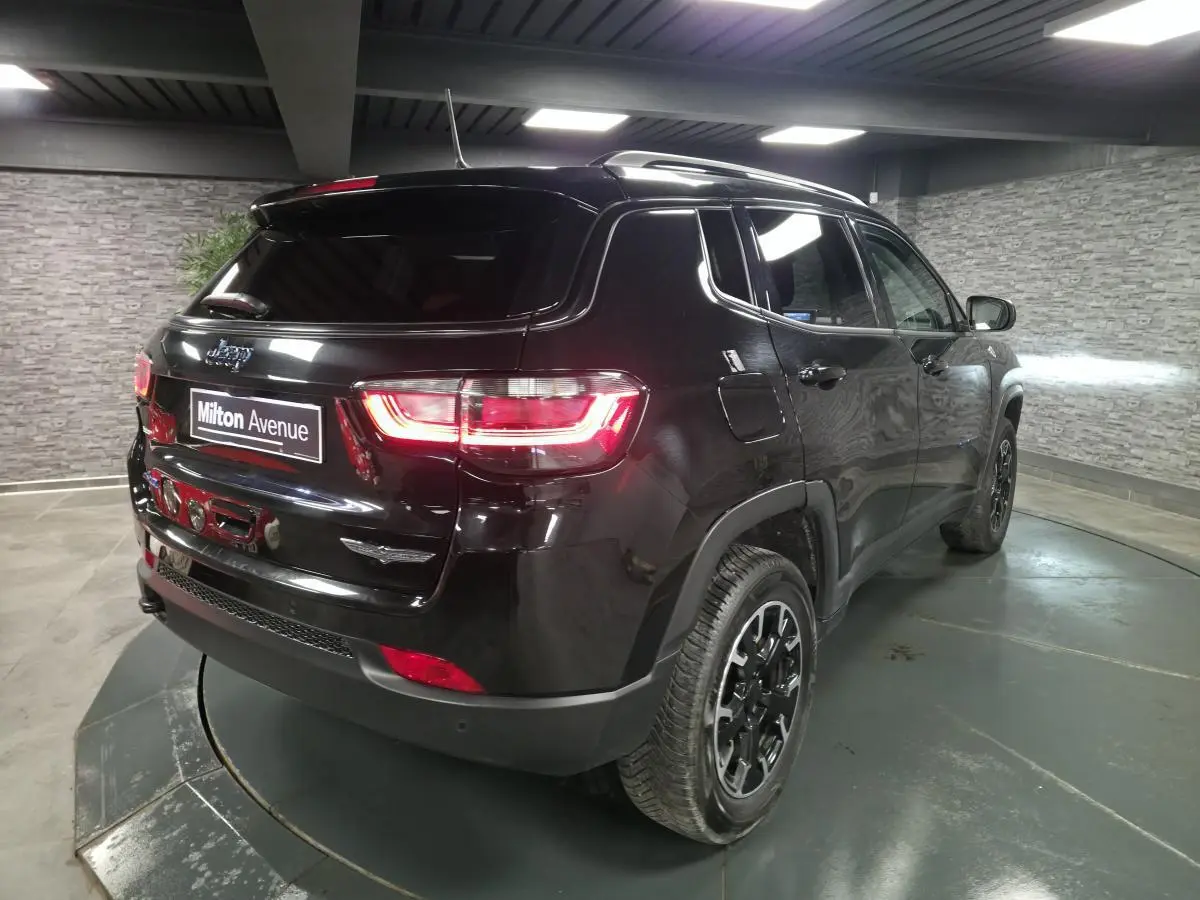 Vue 3/4 arrière droite d'un Jeep Compass noir avec feux arrière allumés et jantes alliage noires en intérieur.